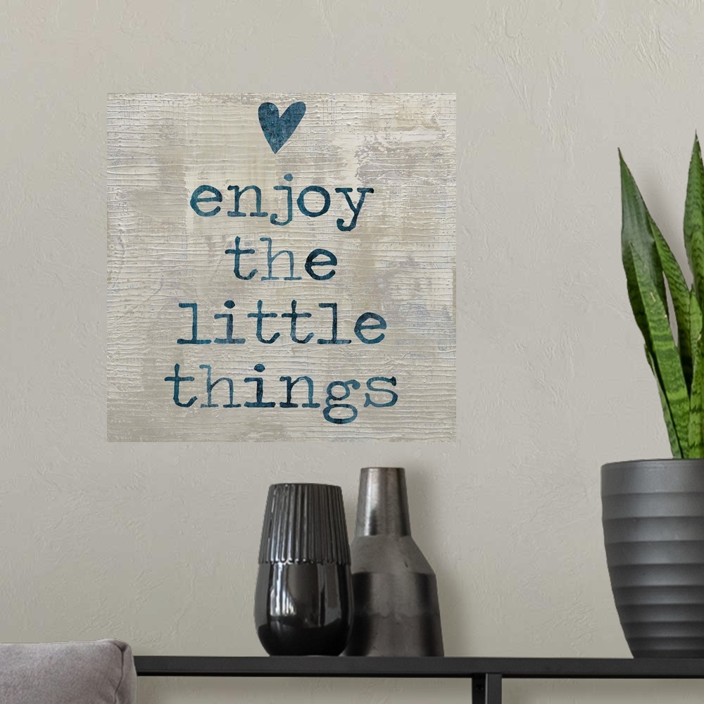 A modern room featuring "enjoy the little things" written in blue with a heart above, on a textured neutral colored backg...