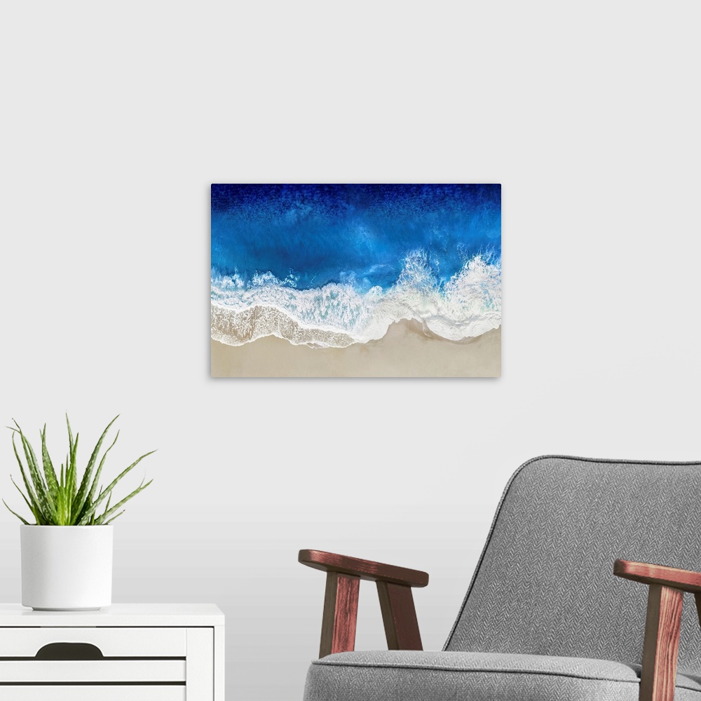 A modern room featuring One artwork in a series of aerial shots of a beach as dark blue waves break upon the shore.