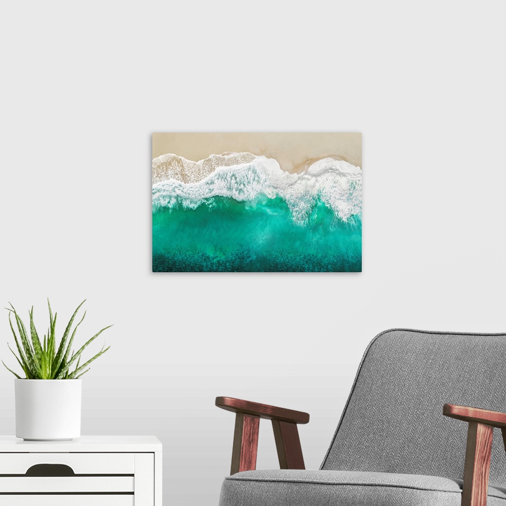 A modern room featuring One artwork in a series of aerial shots of a beach as teal waves break upon the shore.