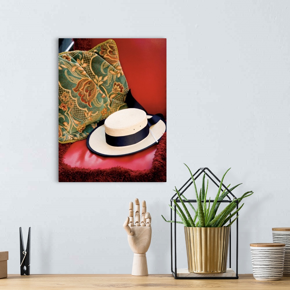 A bohemian room featuring A photograph of a white straw hat sitting on a red leather bench with a floral pillow.