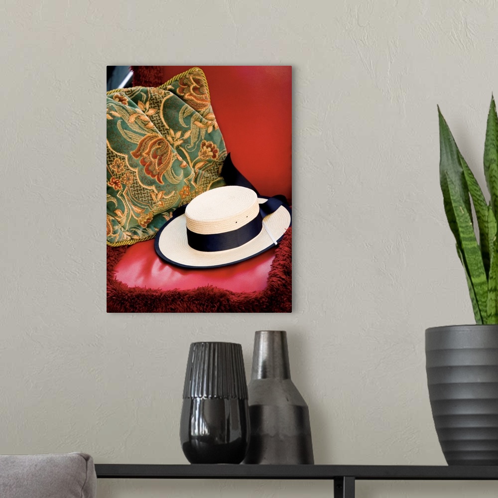 A modern room featuring A photograph of a white straw hat sitting on a red leather bench with a floral pillow.