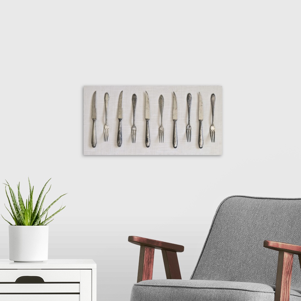 A modern room featuring Photograph of a row of silver antique forks and knifes on a linen cloth.