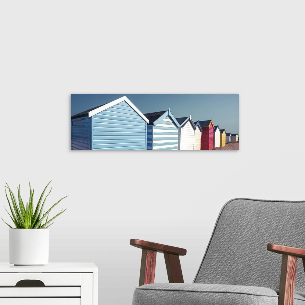 A modern room featuring A panoramic image of a long line of colorful beach huts on a clear day.