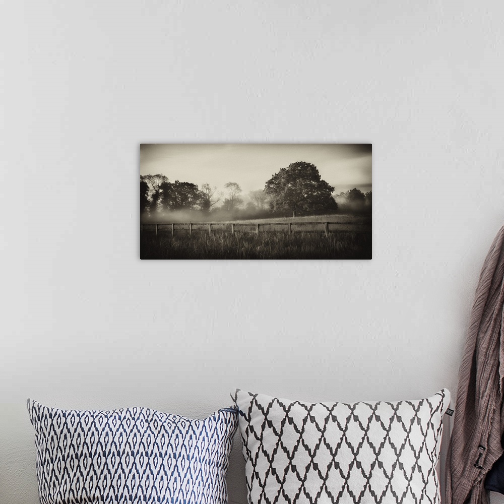 A bohemian room featuring A horizontal photograph of a country field with a wooden fence and mist over trees in the distance.