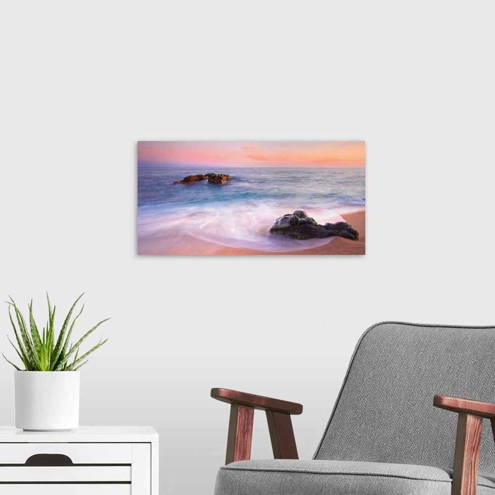 A modern room featuring Panoramic image of gentle waves on a rocky seashore with a vibrant pink sunset.