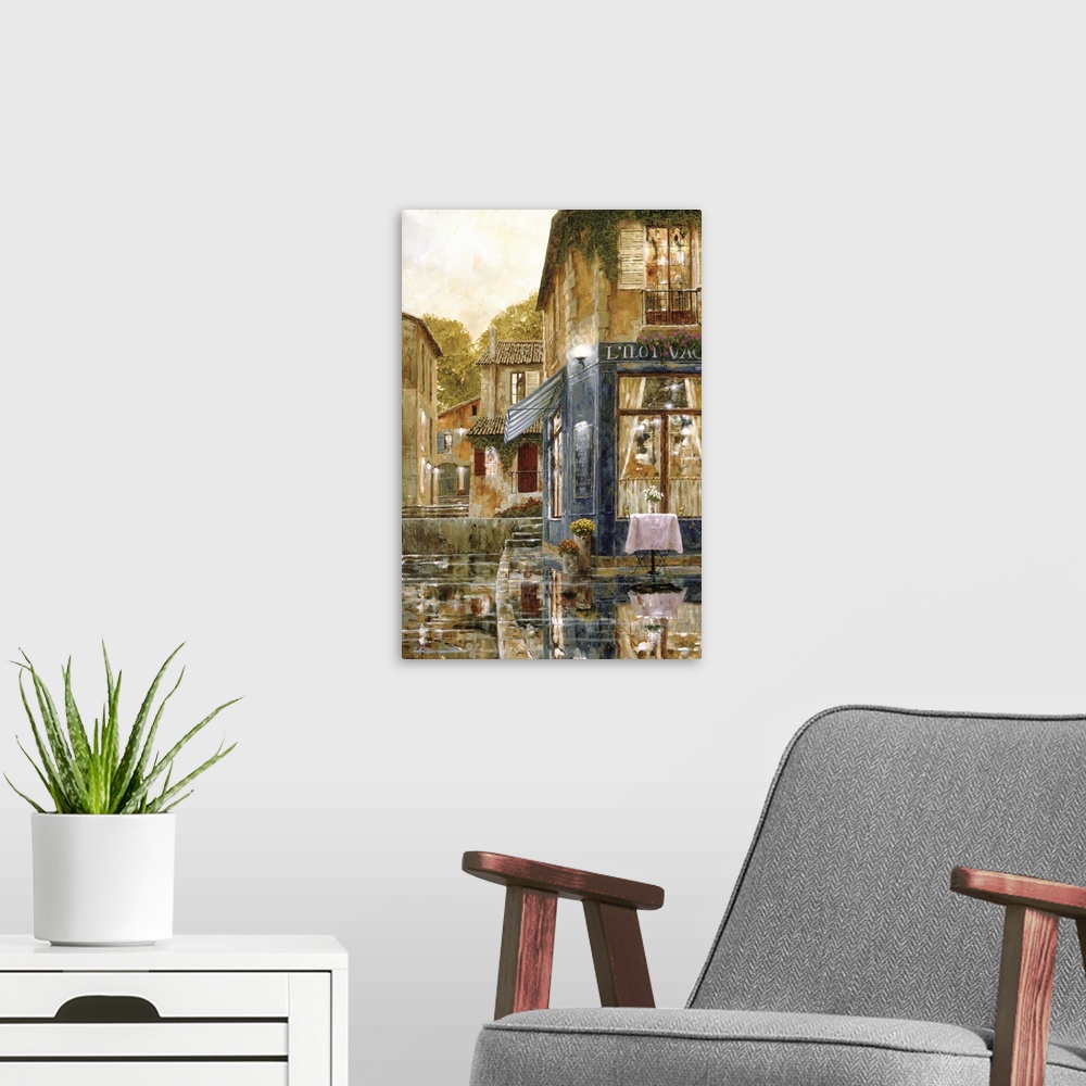 A modern room featuring Vertical artwork of a evening street scene in Europe of a single table outside of a restaurant wi...