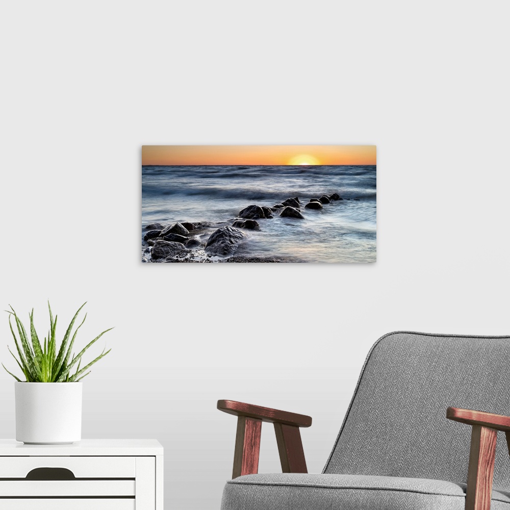 A modern room featuring Photograph of a line of rocks in the surf of a beach during sunset.