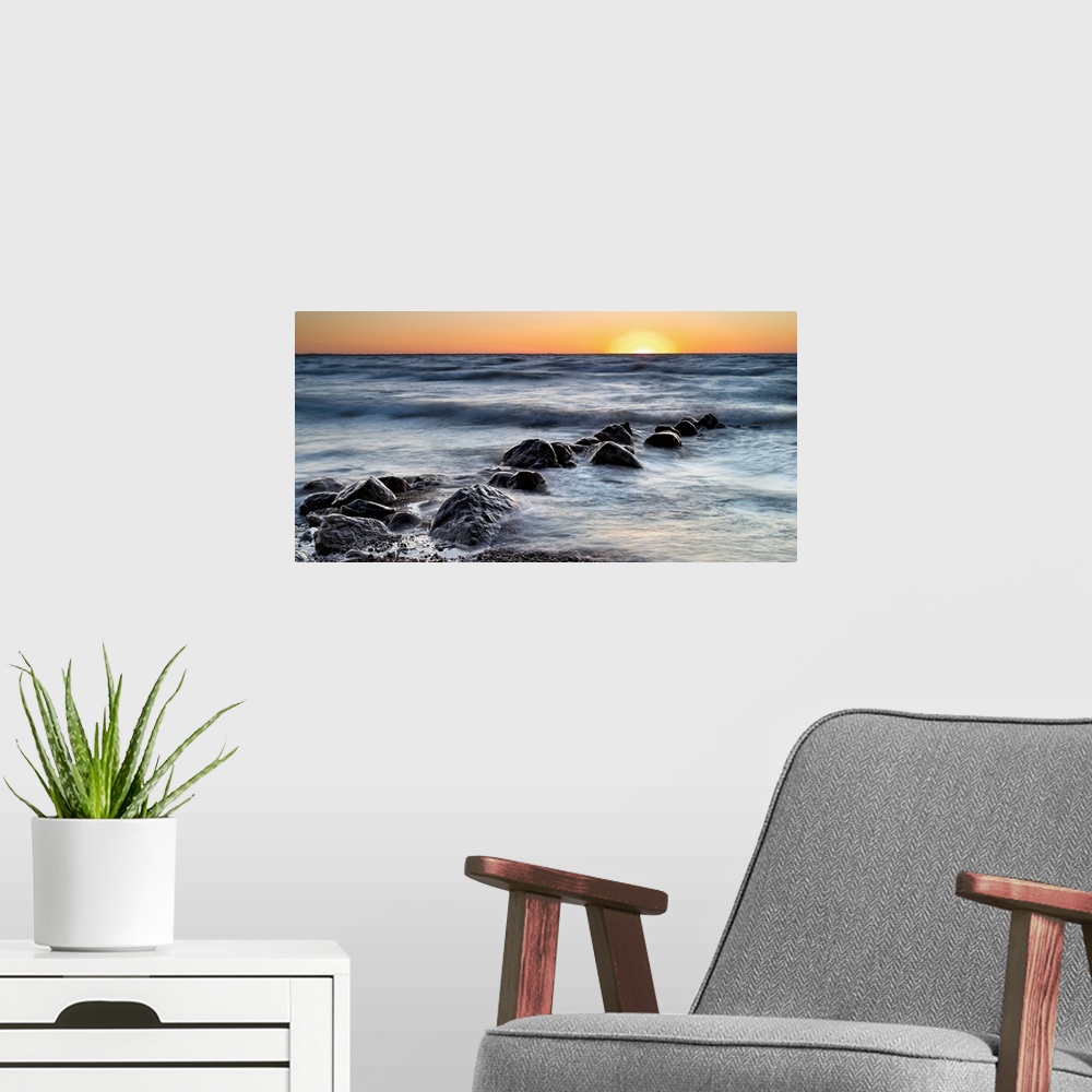 A modern room featuring Photograph of a line of rocks in the surf of a beach during sunset.