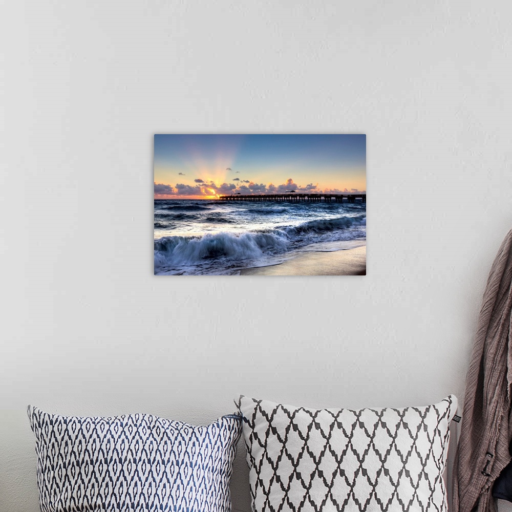 A bohemian room featuring A horizontal photograph of crashing waves on a beach with a sunset and pier in the background.