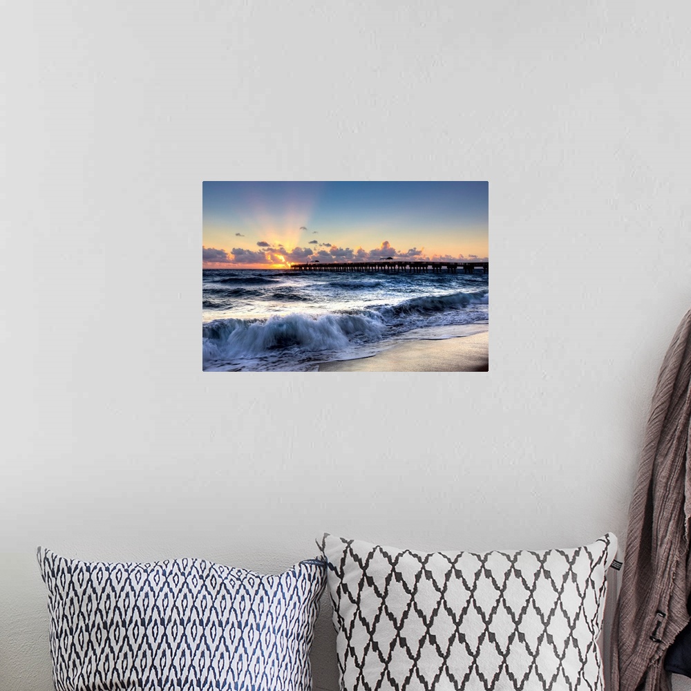 A bohemian room featuring A horizontal photograph of crashing waves on a beach with a sunset and pier in the background.