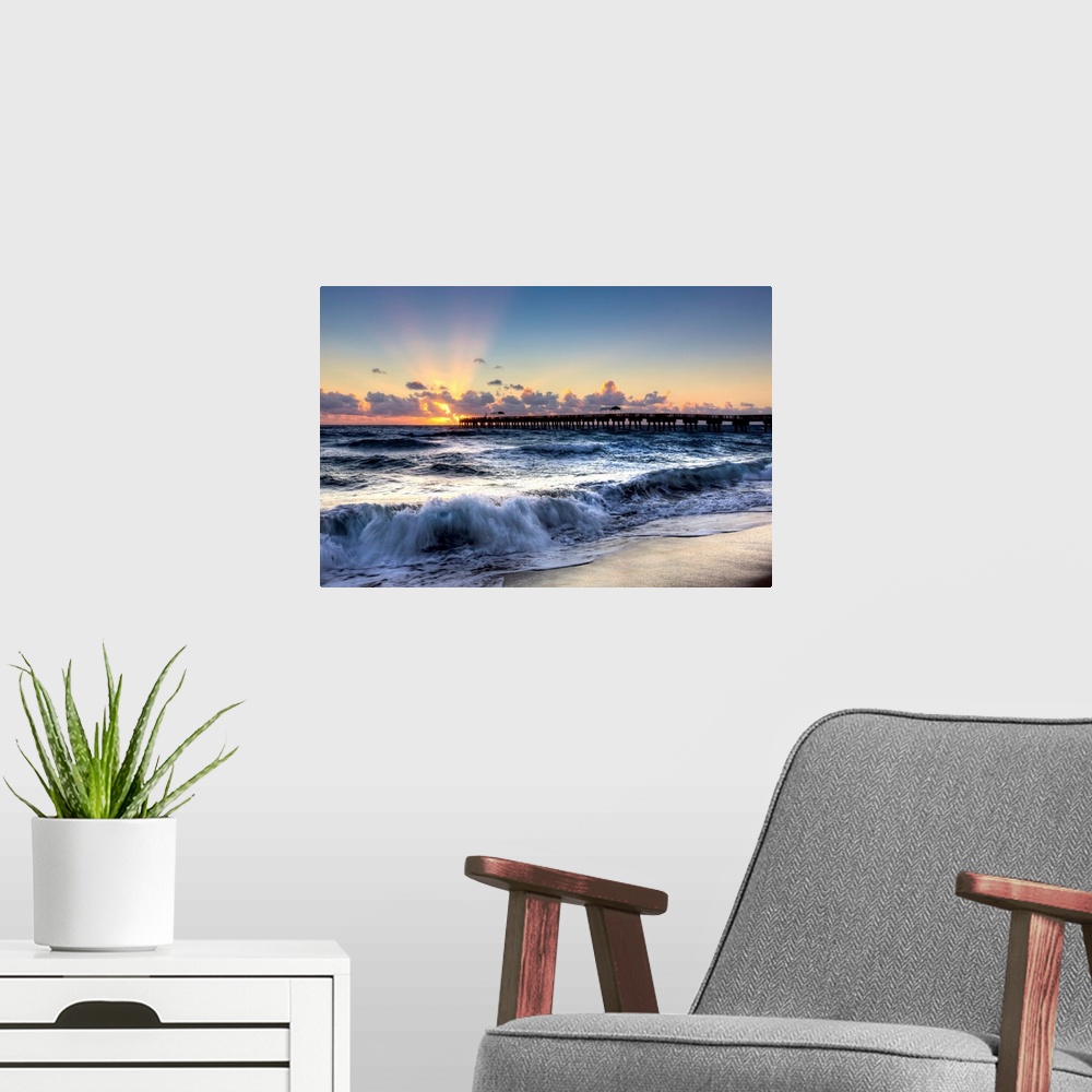 A modern room featuring A horizontal photograph of crashing waves on a beach with a sunset and pier in the background.