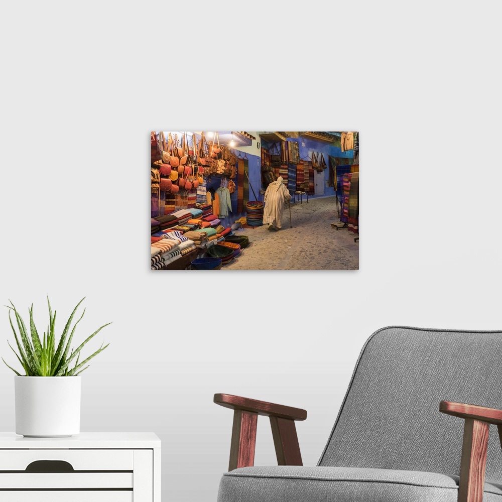 A modern room featuring Africa, Morocco. An elderly man walks past tourist shops along a street in the blue city of Chefc...