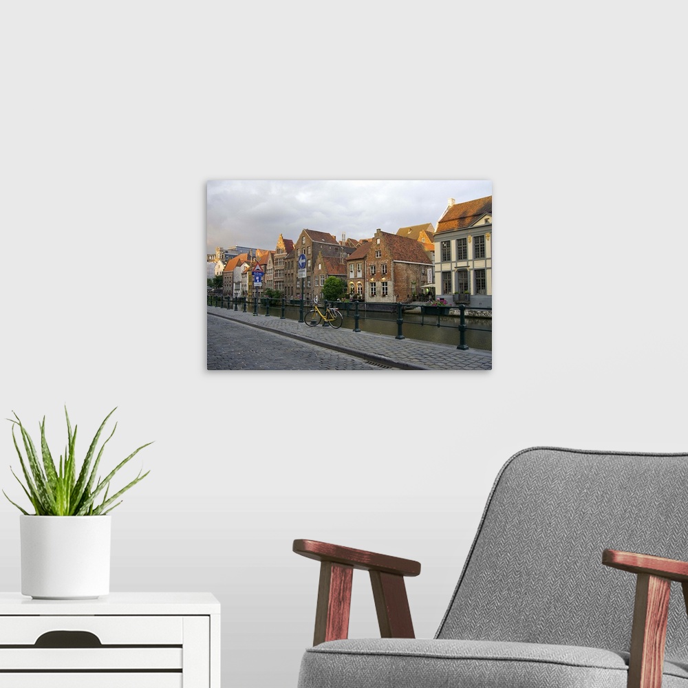 A modern room featuring Europe, Belgium, Ghent.  A bicycle parked on a paved-stone sidewalk by the water, and historic Gh...
