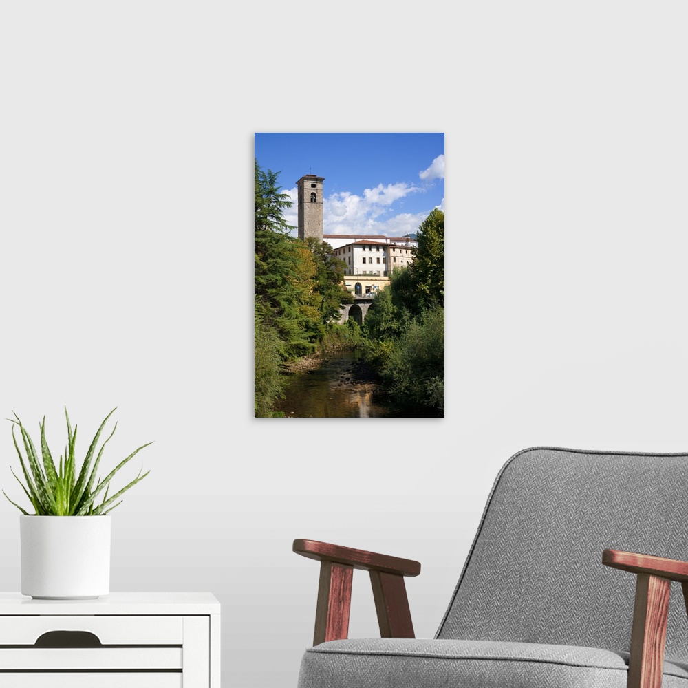 A modern room featuring Castelnuovo di Garfagnana, Tuscany, Italy - Old world buildings as seen behind a small waterway a...
