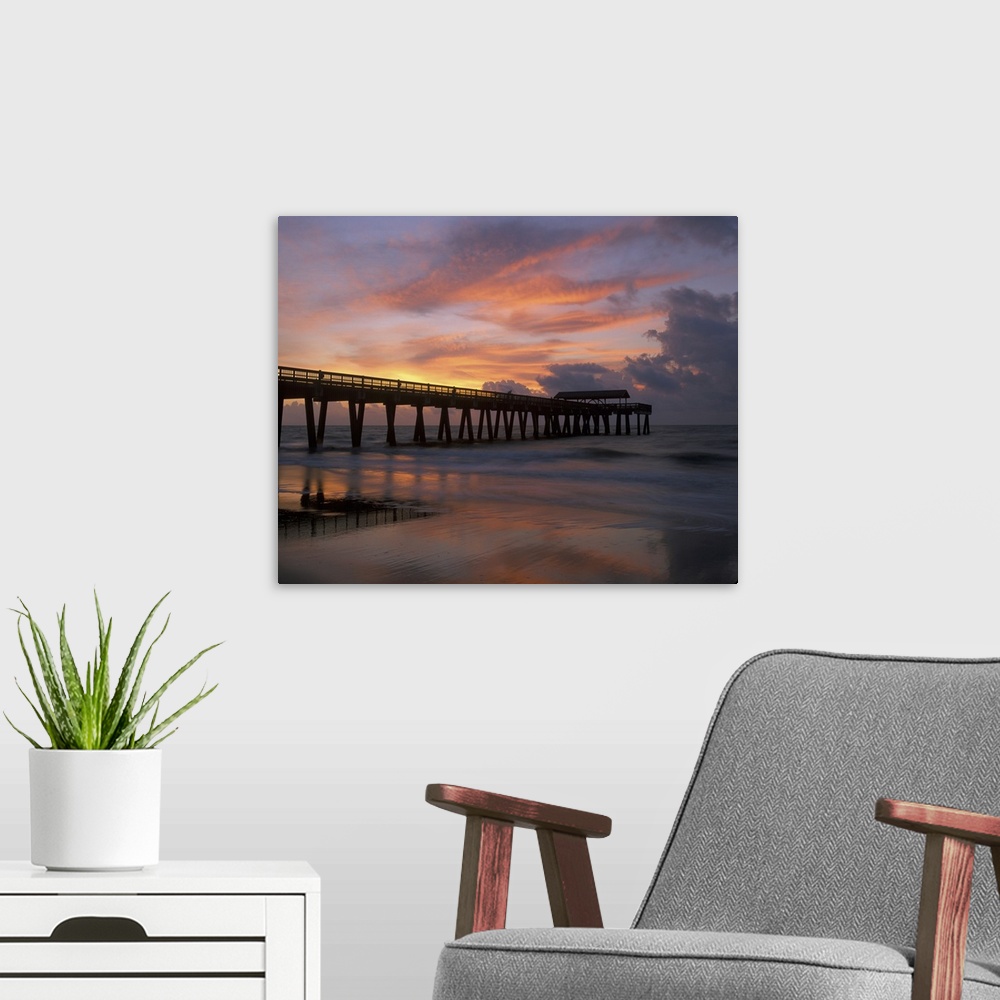 A modern room featuring Georgia Tybee Island, pier at sunrise with reflections of clouds on beach.