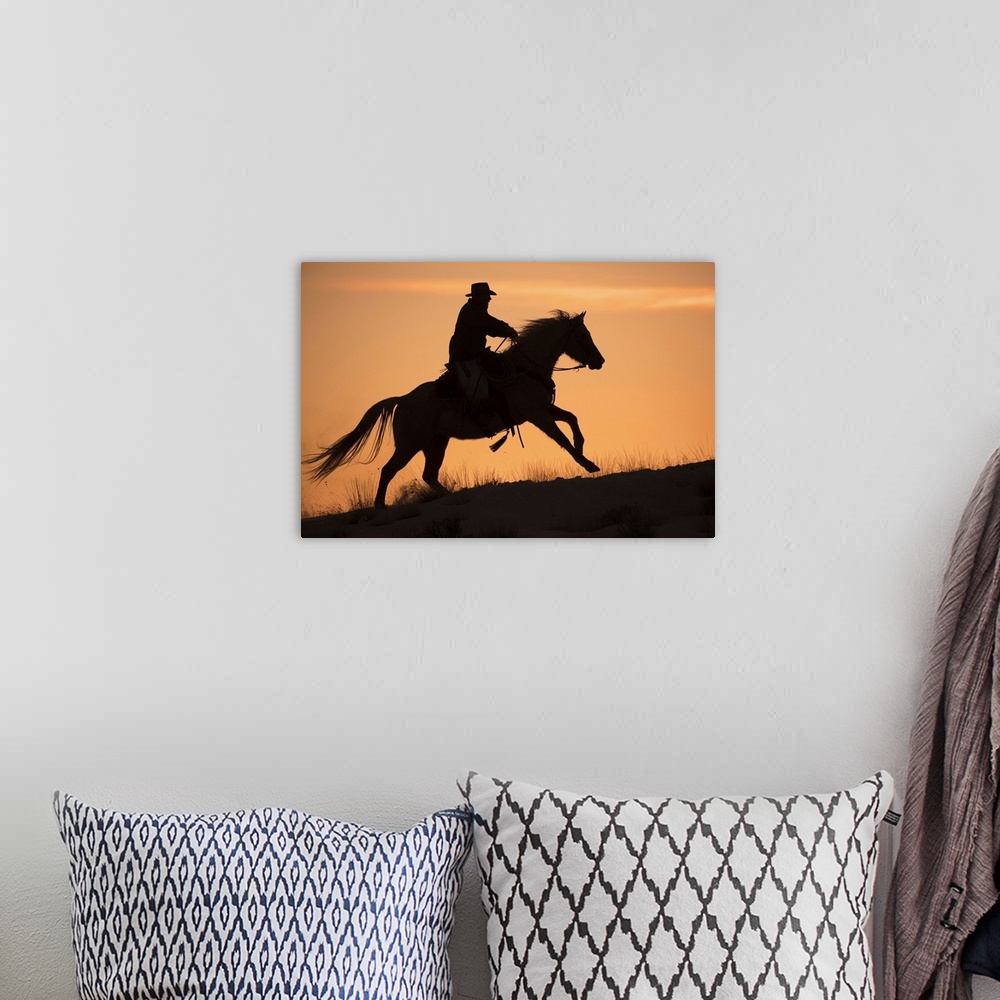 A bohemian room featuring Horse drive in winter on Hideout Ranch, Shell, Wyoming. Cowboy riding his horse silhouetted at su...