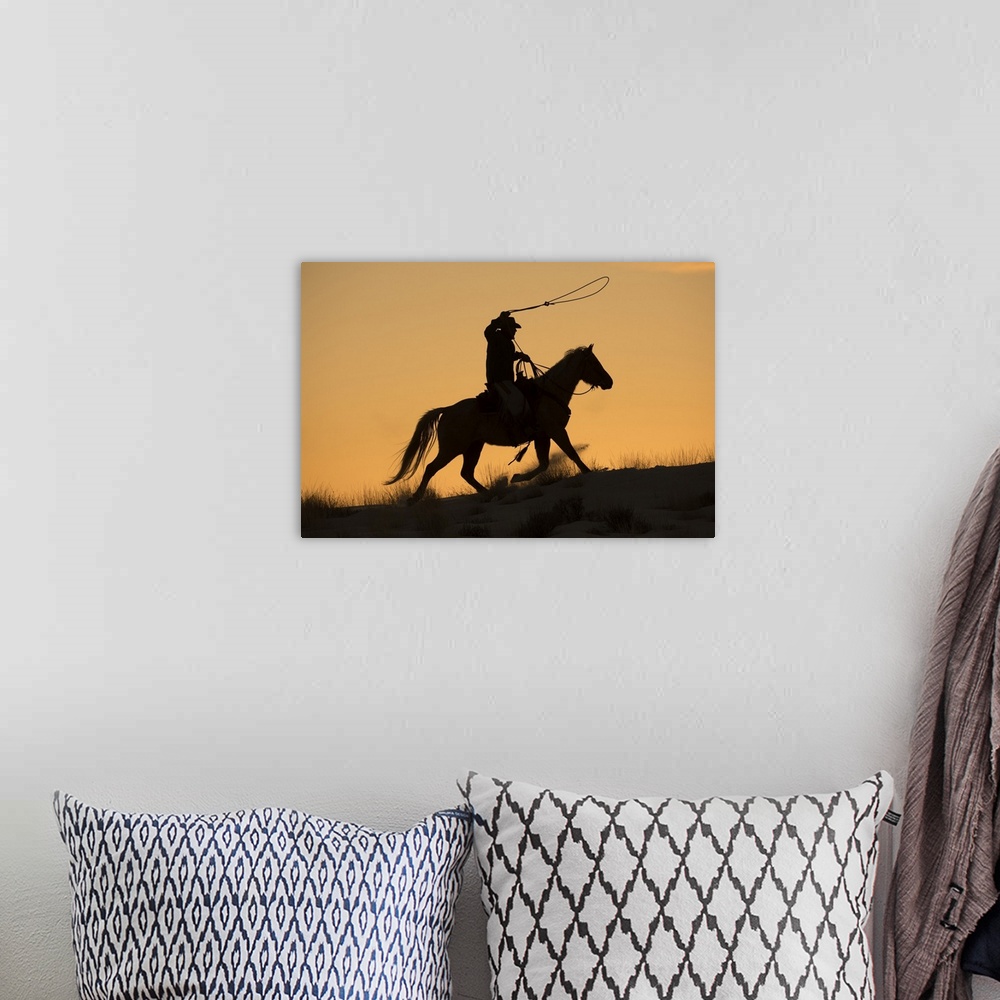 A bohemian room featuring Cowboy horse drive on Hideout Ranch, Shell, Wyoming. Cowboy riding his horse with rope out silhou...