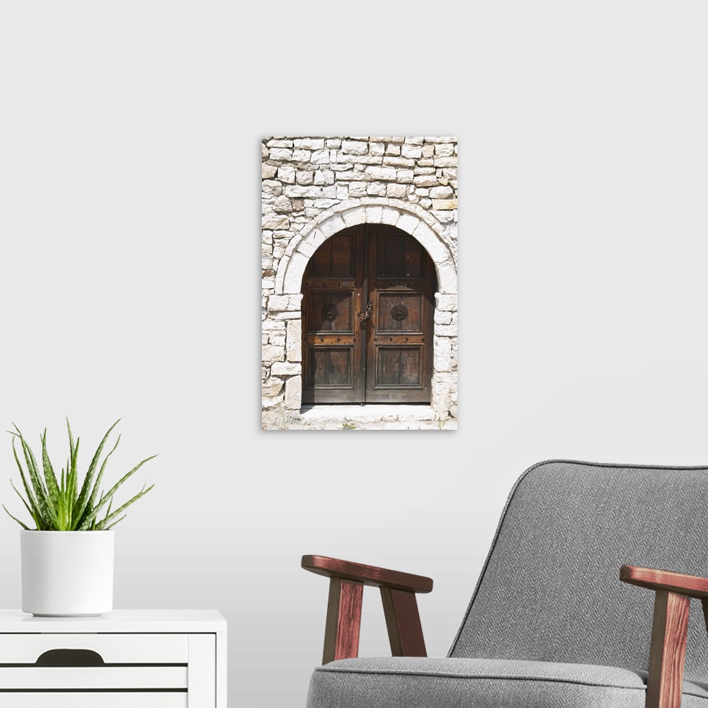 A modern room featuring Stone wall with old wooden door with chain and pad lock. Berat upper citadel old walled city. Alb...