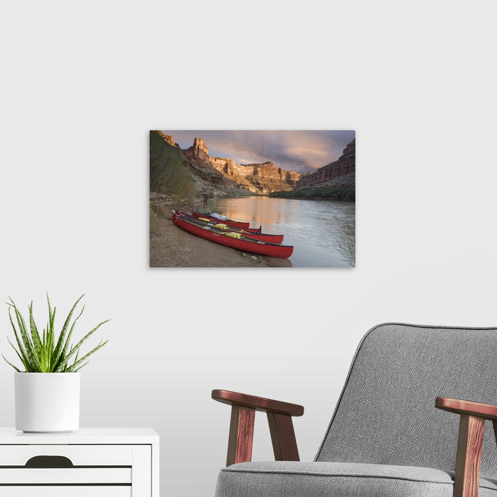A modern room featuring USA, Utah, Canyonlands National Park. Three red canoes rest on bank of Green River.