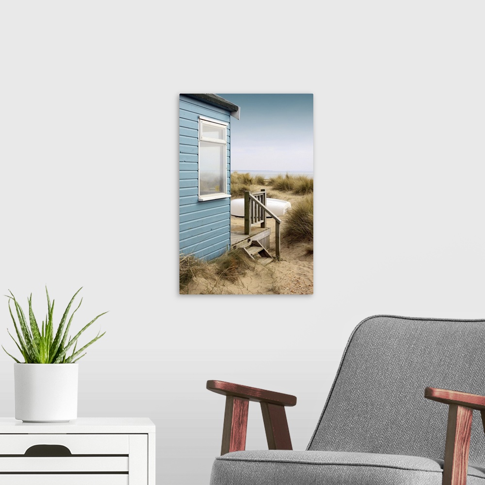 A modern room featuring View of the side of a blue wooden beach hut with a wooden terrace, looking towards the coast/beac...