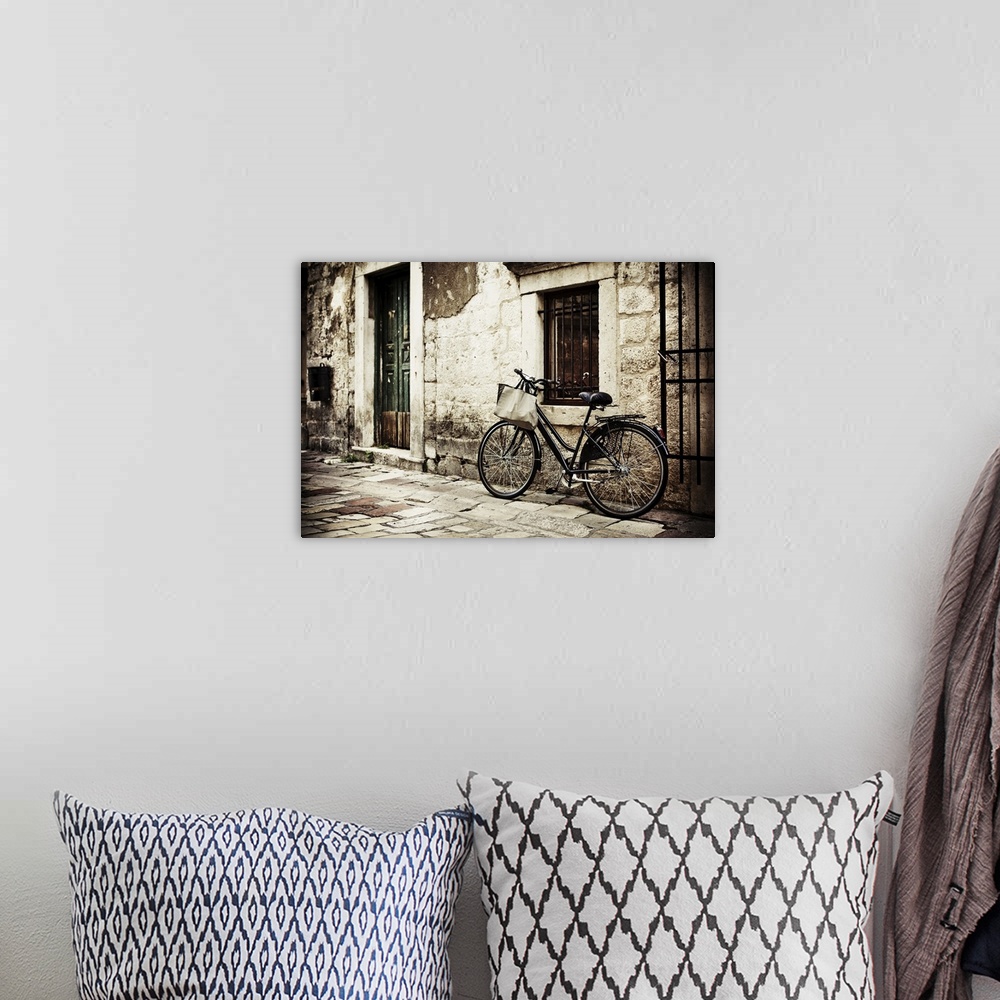 A bohemian room featuring Bicycle with a shopping bag on handle bar, left beside old stone wall.