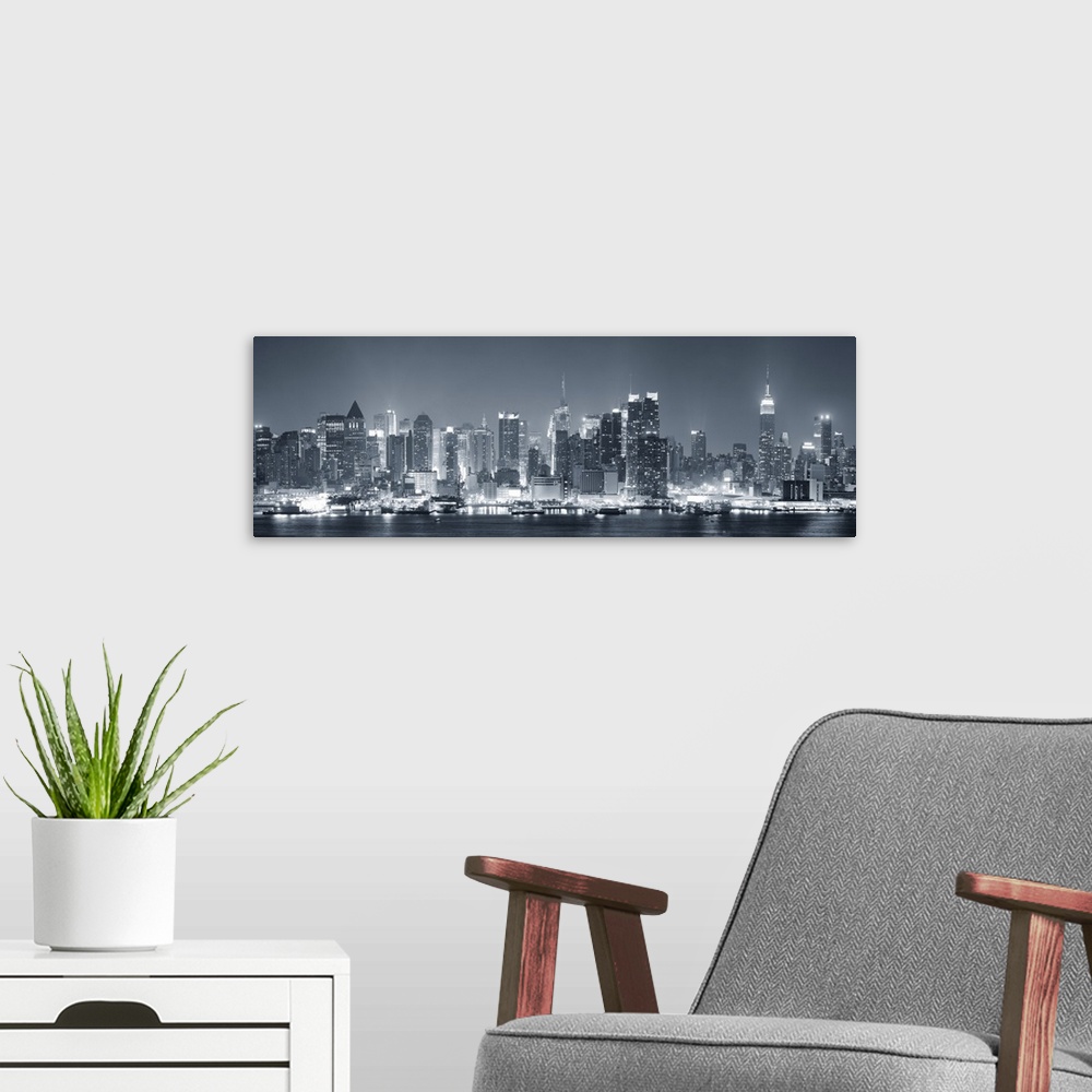 A modern room featuring Manhattan midtown skyline in black and white at night with skyscrapers lit over Hudson River with...