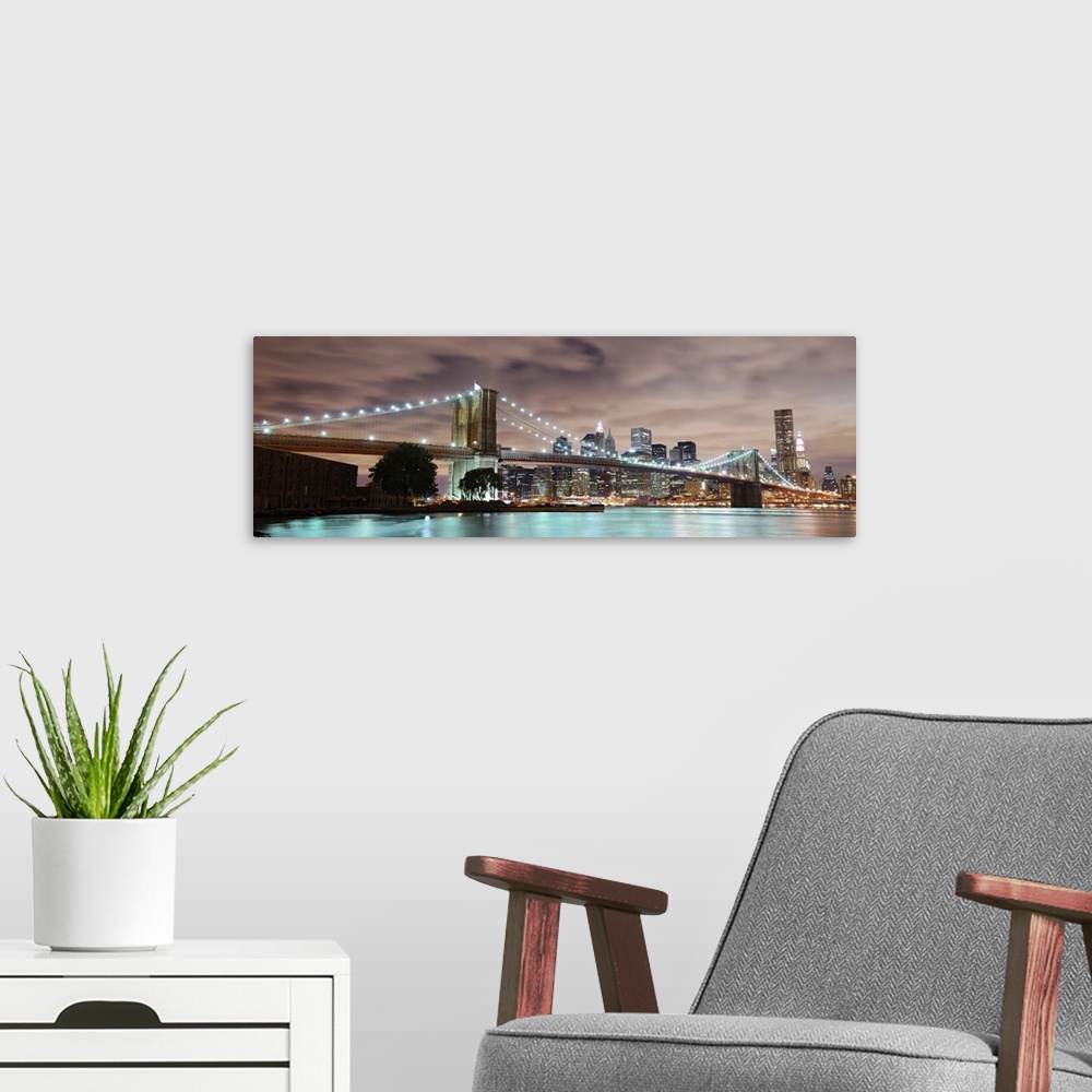 A modern room featuring Panoramic view of Manhattan with Brooklyn Bridge at night with skyscrapers illuminated over the H...