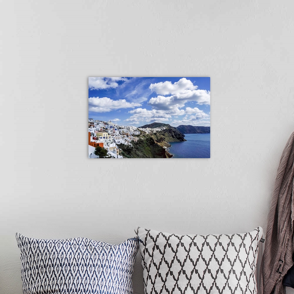A bohemian room featuring White houses near tranquil sea against blue sky with clouds in Greece.