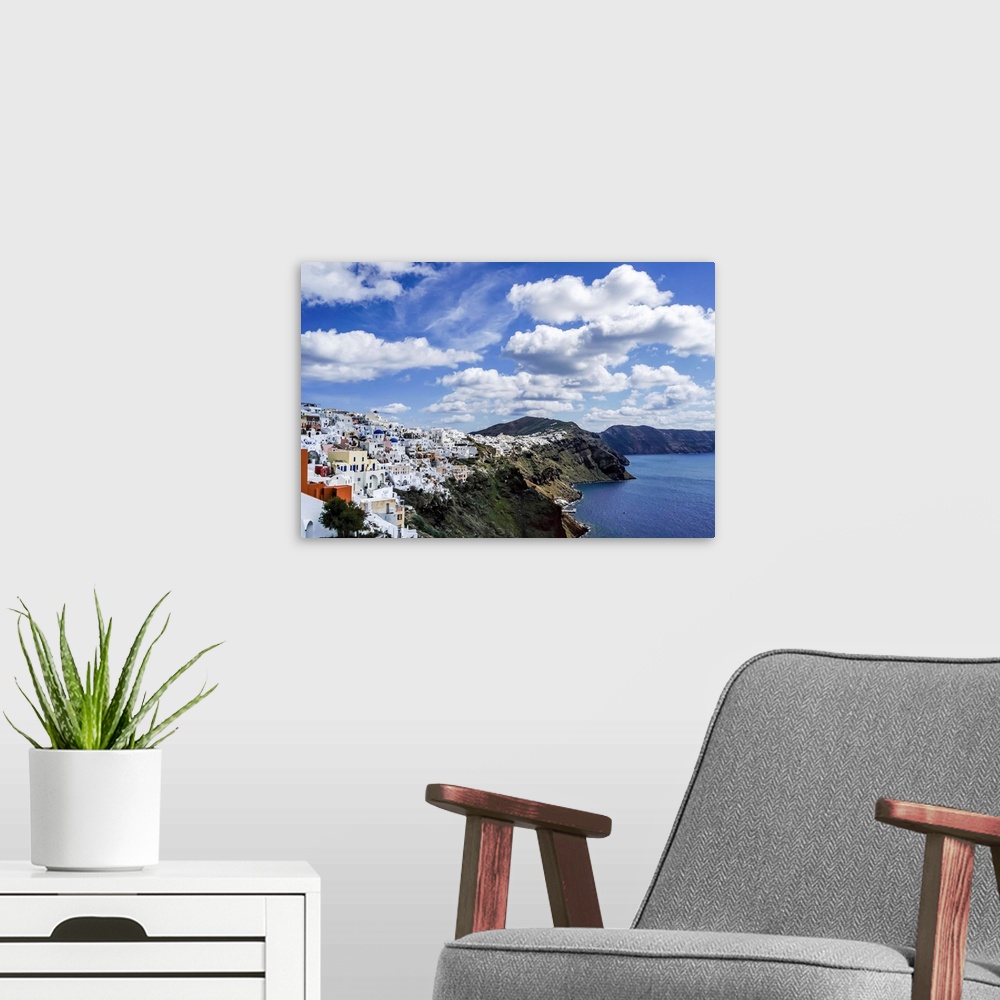 A modern room featuring White houses near tranquil sea against blue sky with clouds in Greece.