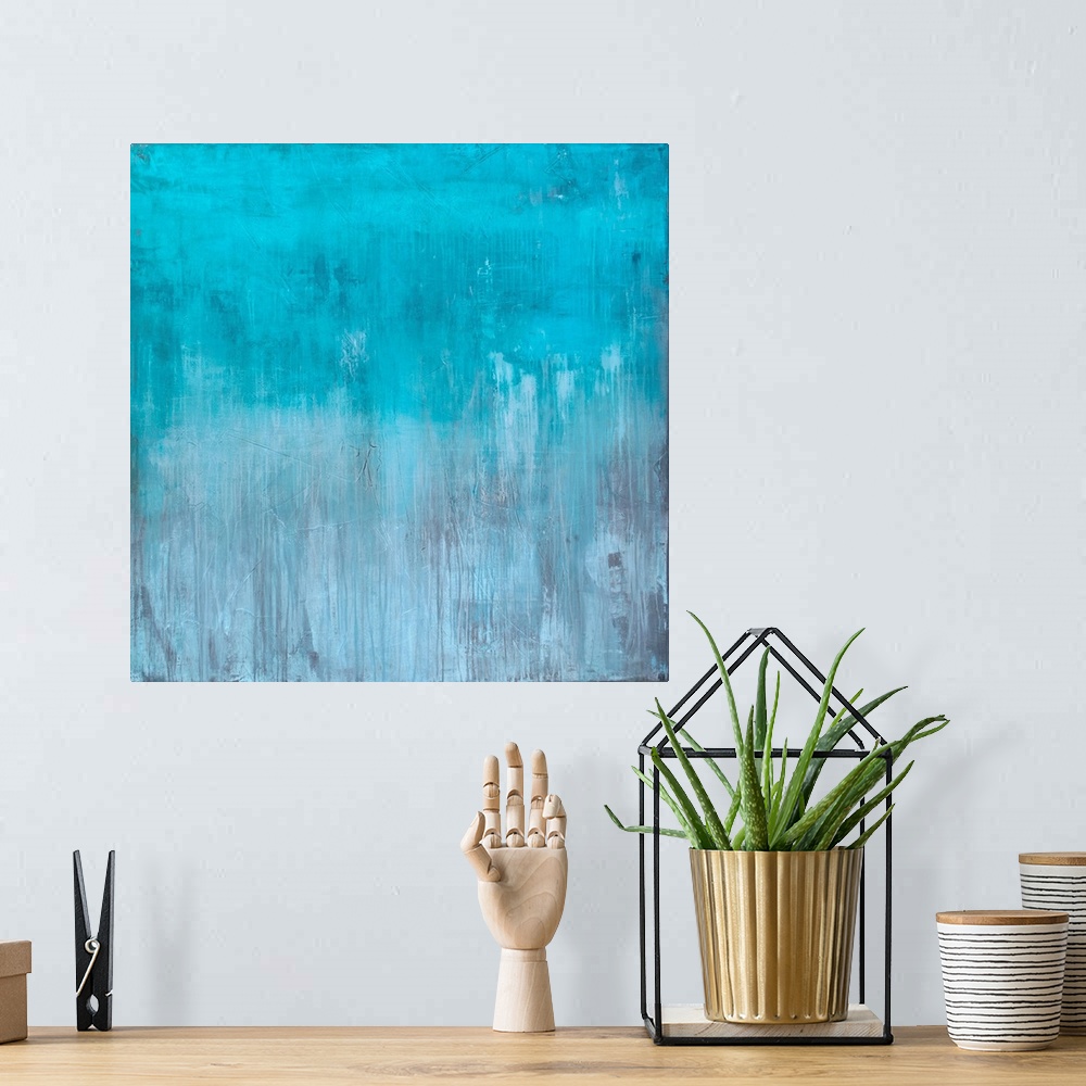 A bohemian room featuring Square abstract painting created with light blue turning into gray towards the bottom with streak...