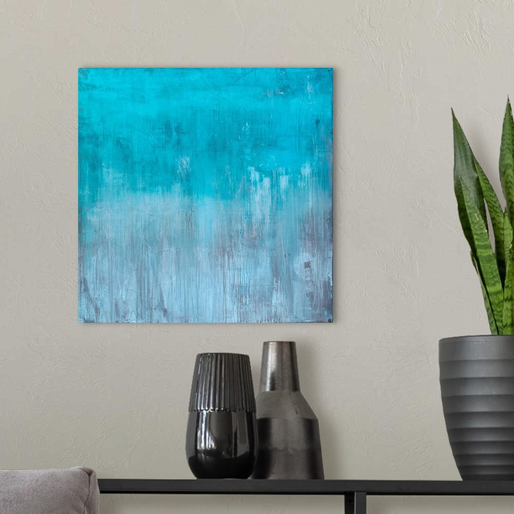 A modern room featuring Square abstract painting created with light blue turning into gray towards the bottom with streak...