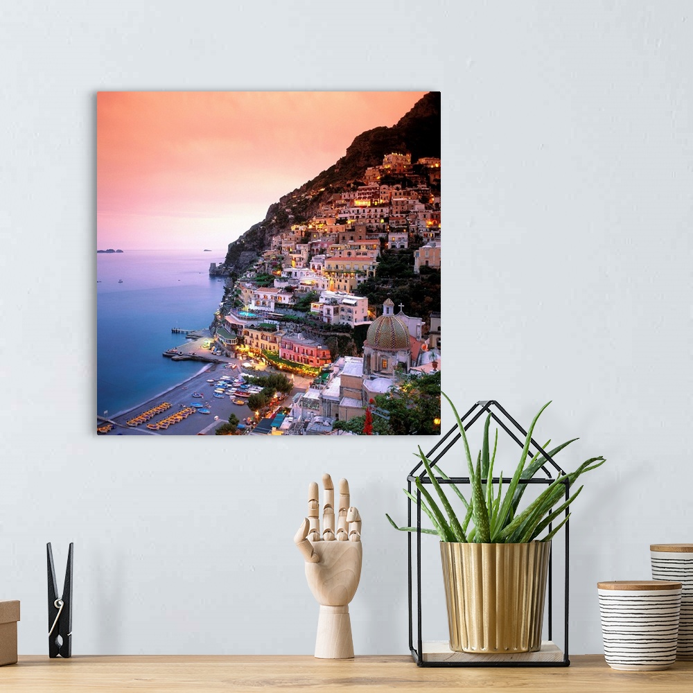 A bohemian room featuring A square shaped photograph of the charming Italian town of Positano at sunset. Built into the cli...