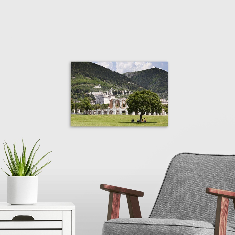 A modern room featuring Italy, Umbria, People under a tree with the Roman theatre and Palazzo dei Consoli