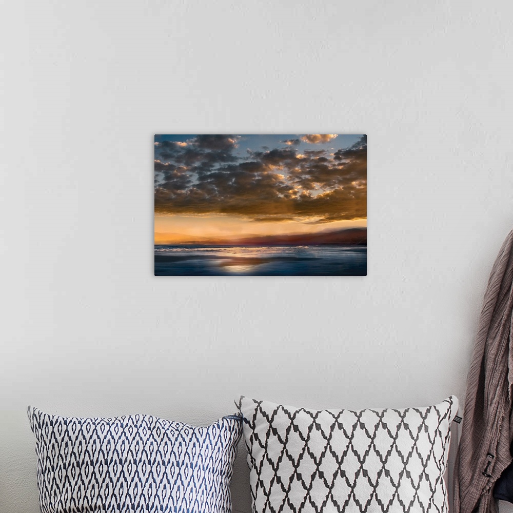 A bohemian room featuring Seascape photograph with mountains in the distance and a cloudy sky at sunset.
