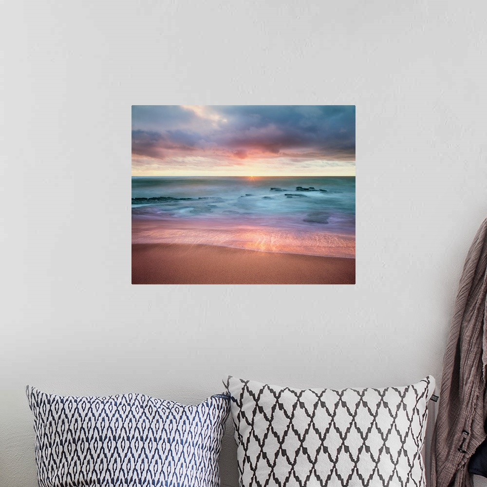 A bohemian room featuring Colorful long exposure photograph a rocky ocean shore with the sun on the horizon in shades of bl...
