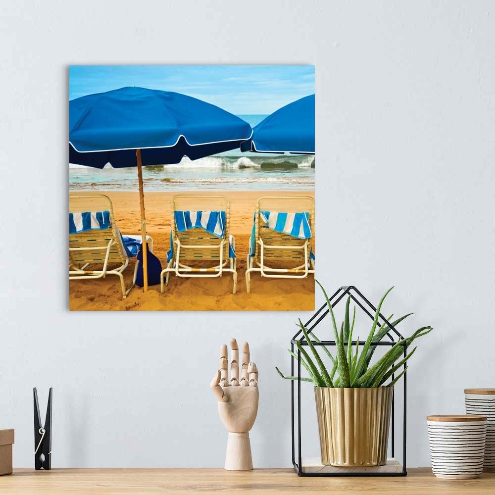 A bohemian room featuring Square photograph of three beach chairs with blue umbrellas lined up right in front of the ocean.