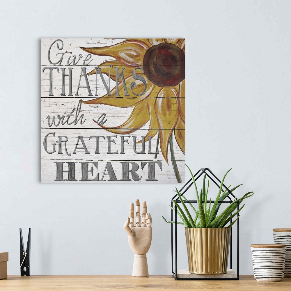 A bohemian room featuring "Give thanks with a grateful heart" handwritten on white shiplap background and sunflower.