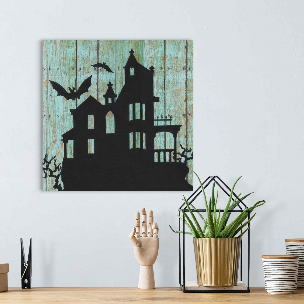 A bohemian room featuring A decorative Halloween painting of a haunted house with two bats flying around it on an aged, blu...
