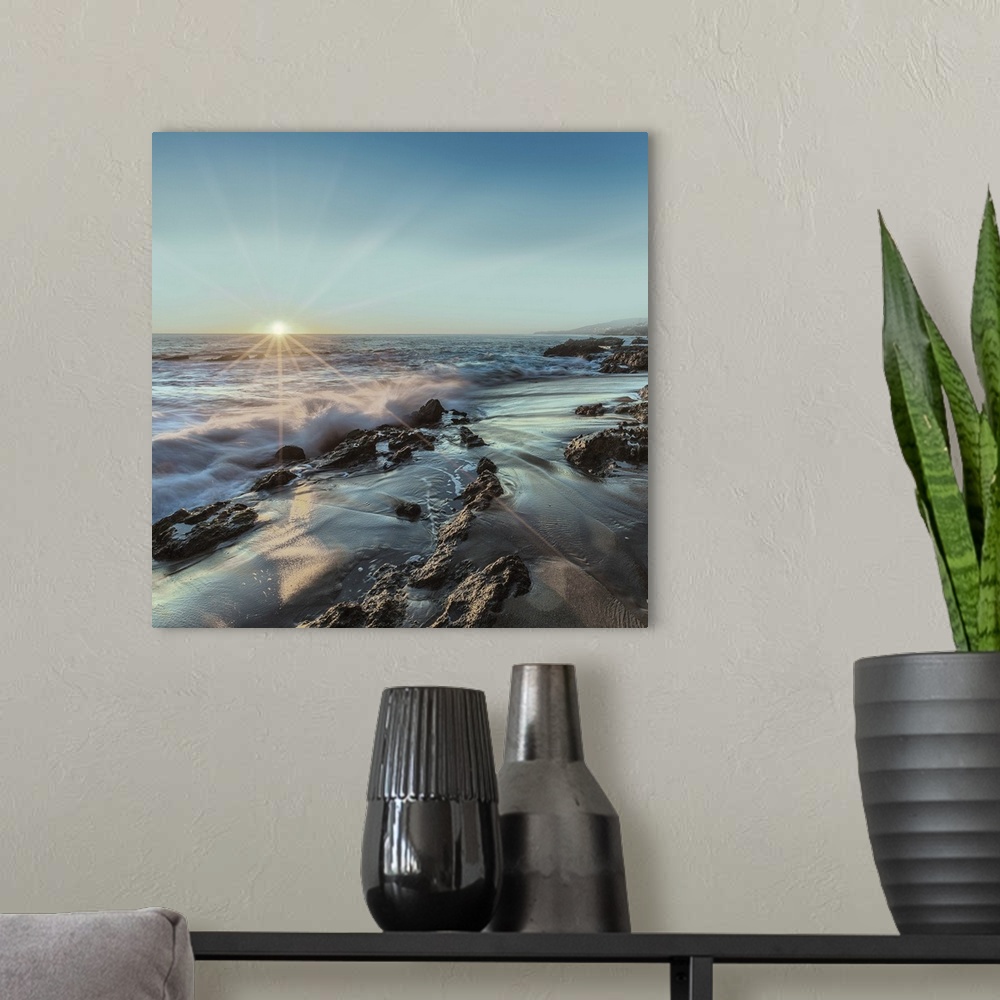 A modern room featuring Square photograph of ocean waves crashing on a rocky shore with the sun setting on the horizon li...
