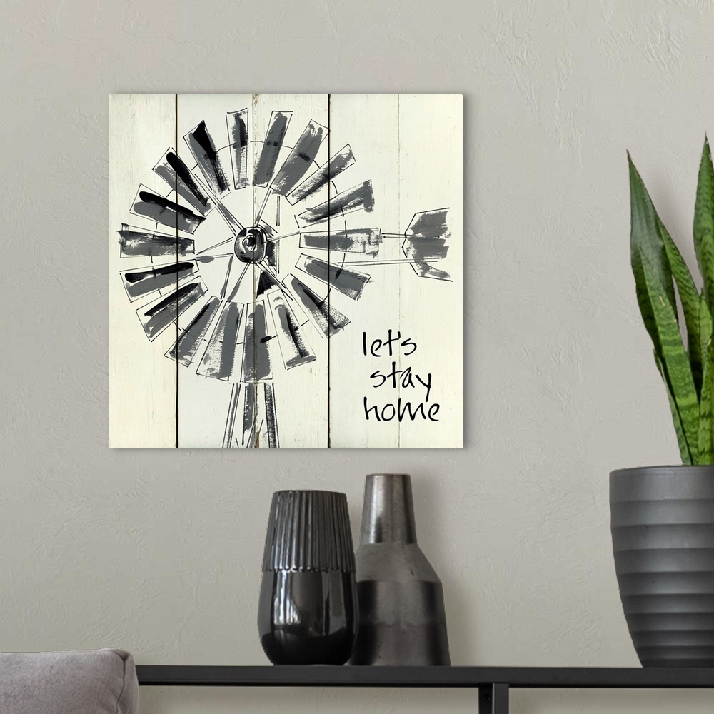 A modern room featuring 'Let's Stay Home' written on a square shiplap background with an illustration of a windmill.
