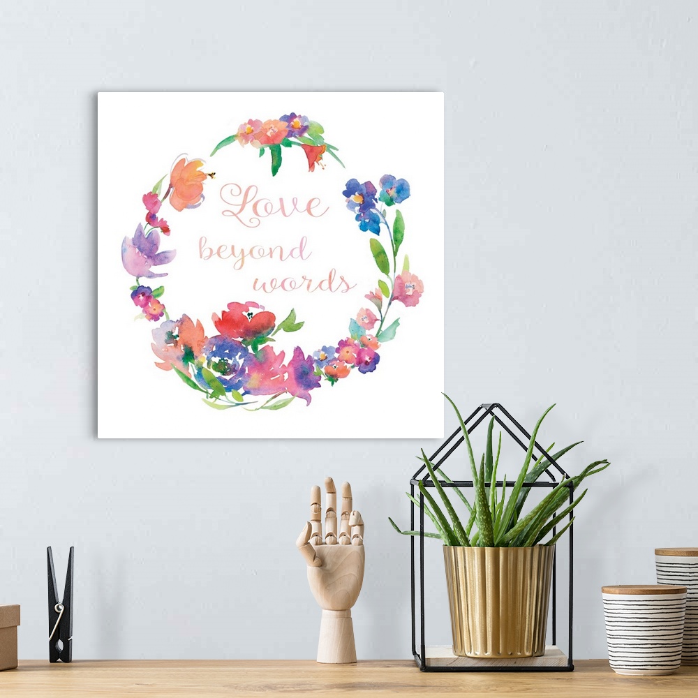 A bohemian room featuring "Love Beyond Words" written in cursive inside of a watercolor floral wreath on a white square bac...