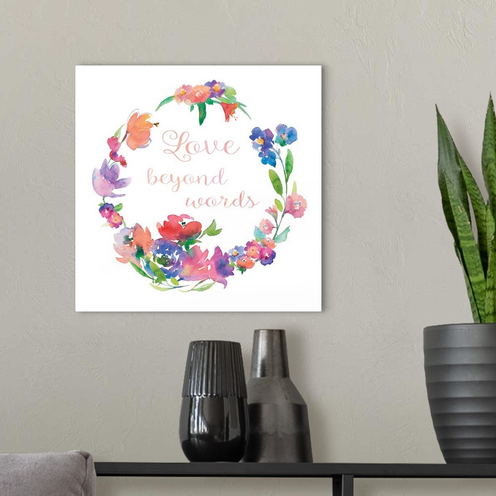 A modern room featuring "Love Beyond Words" written in cursive inside of a watercolor floral wreath on a white square bac...