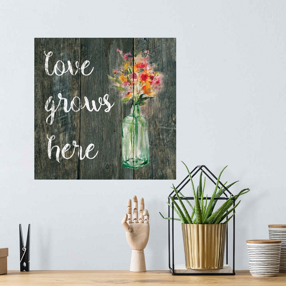 A bohemian room featuring "Love Grows Here" written in white on a faux wood background with pink and orange flowers in a gl...
