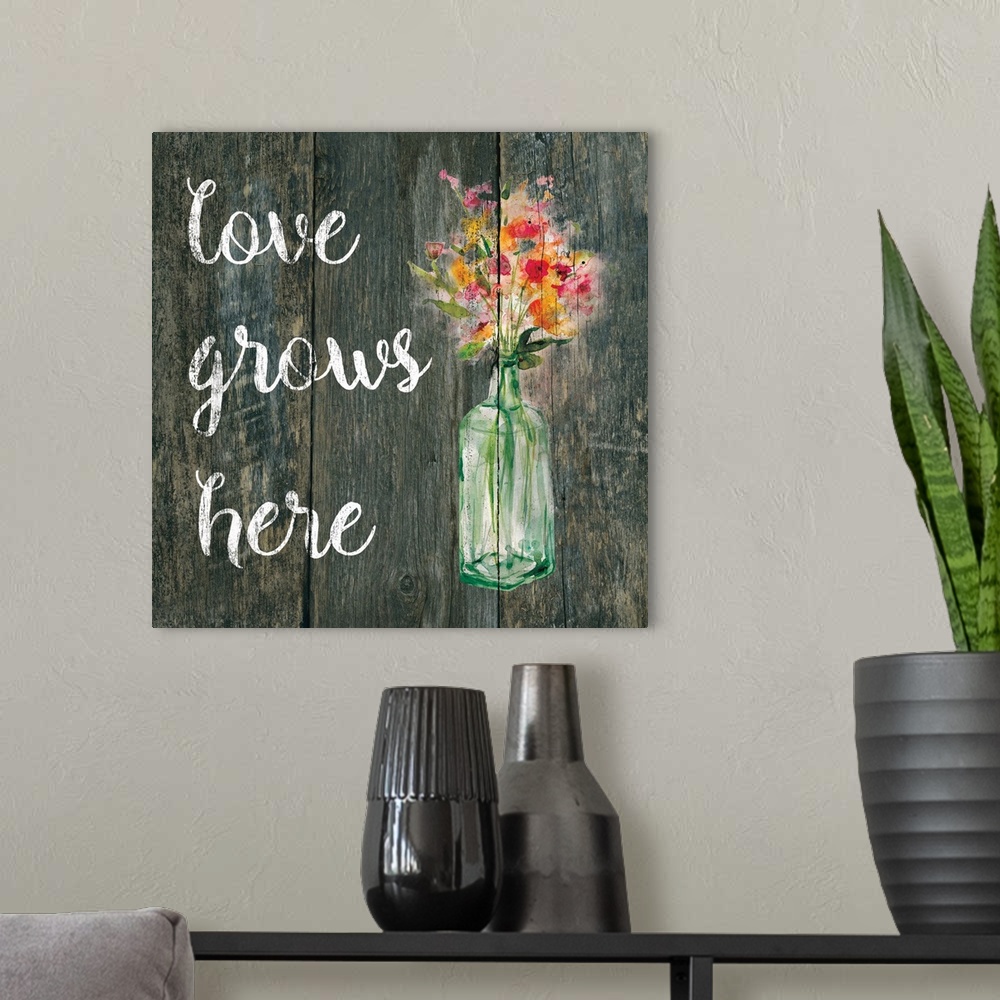 A modern room featuring "Love Grows Here" written in white on a faux wood background with pink and orange flowers in a gl...