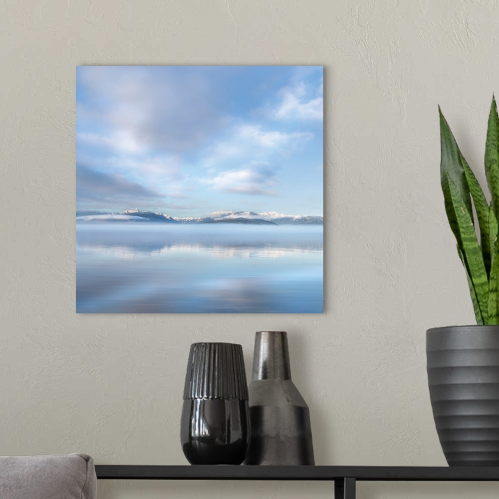 A modern room featuring Square photograph of a snow capped mountain range in the distance with fluffy clouds above reflec...