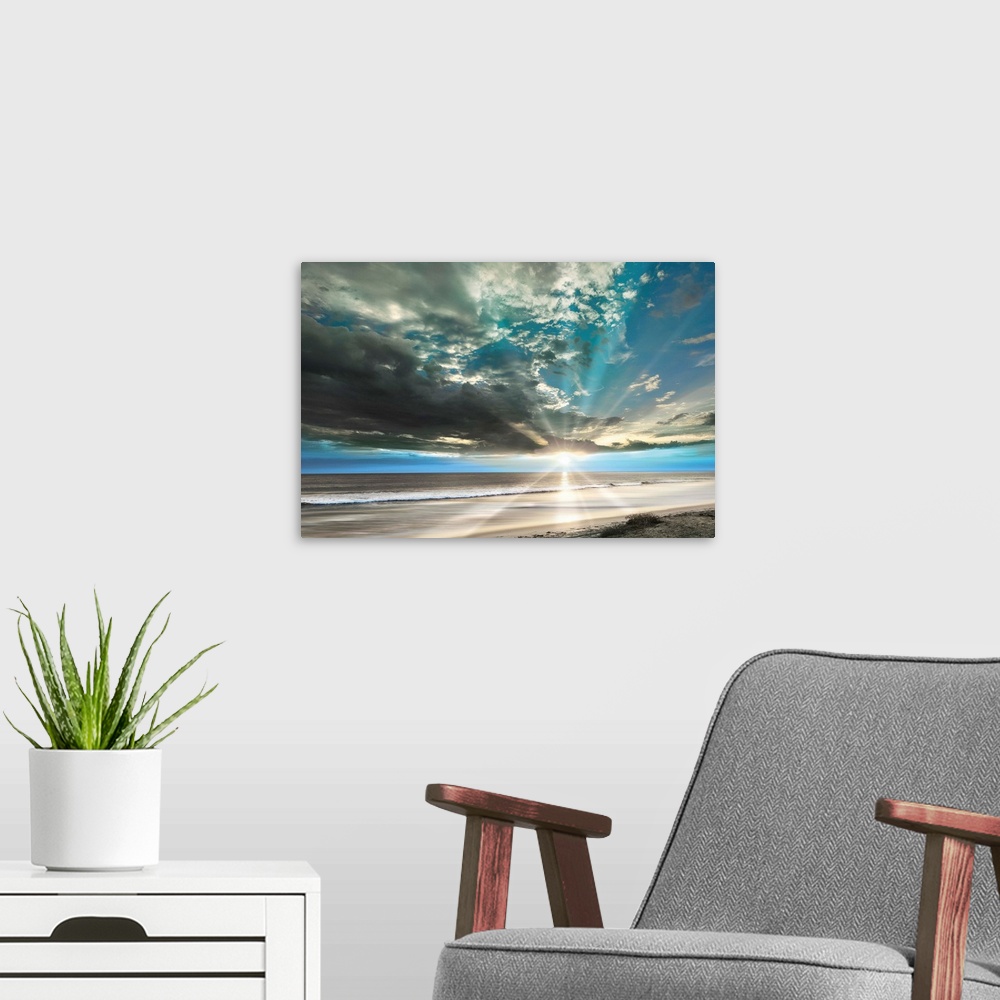 A modern room featuring Stunning landscape photograph of the sun beaming over an empty beach with contrasting clouds in t...