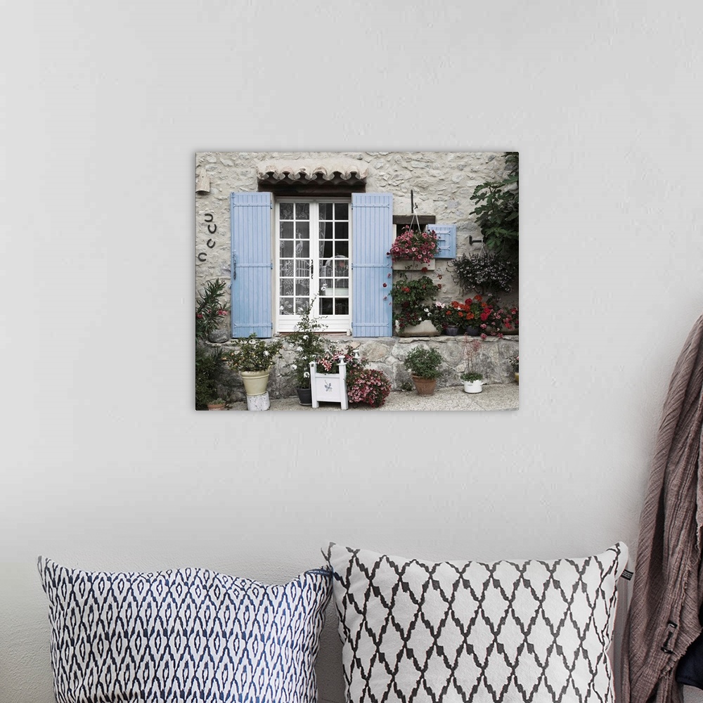 A bohemian room featuring Photograph of a window with blue shutters on a house with potted plants surrounding it.