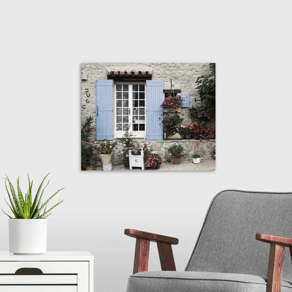 A modern room featuring Photograph of a window with blue shutters on a house with potted plants surrounding it.