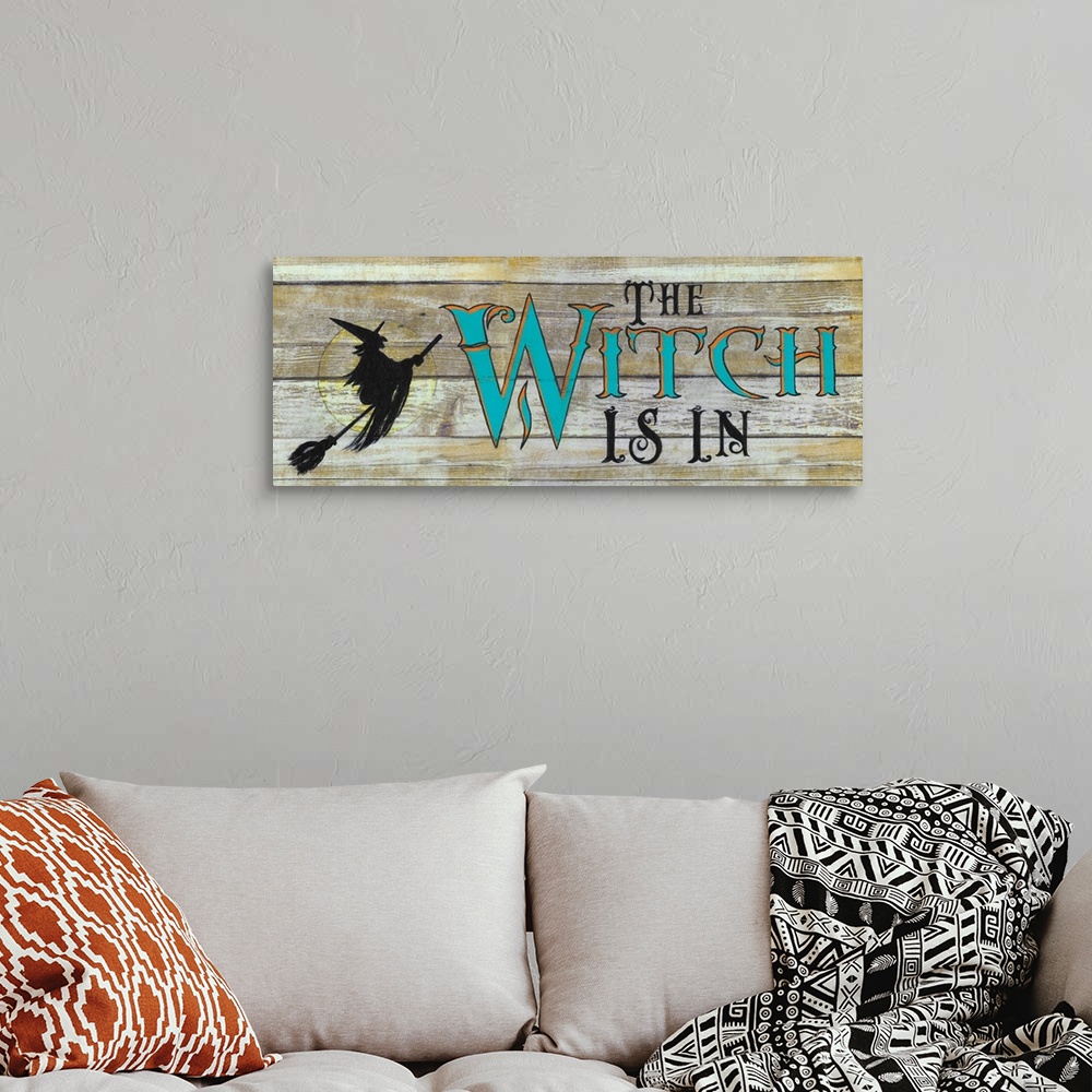 A bohemian room featuring A decorative Halloween painting of a witch riding a broomstick over the moon with the phrase ?The...