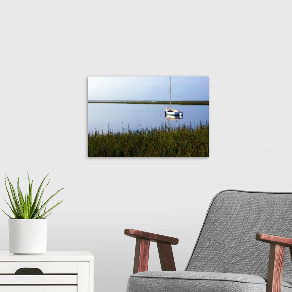A modern room featuring A landscape photograph of a sailboat anchored in still waters surrounded by marshy grasses on the...